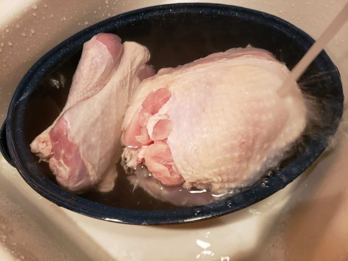 Washing raw turkey and legs in roasting pan in the sink under cold water.