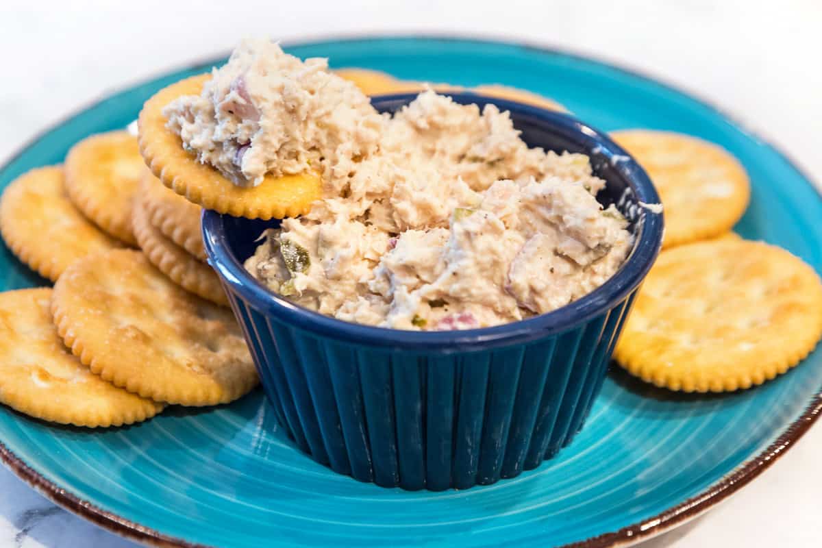 Close up of classic tuna salad recipe in a bowl and on a Ritz cracker.