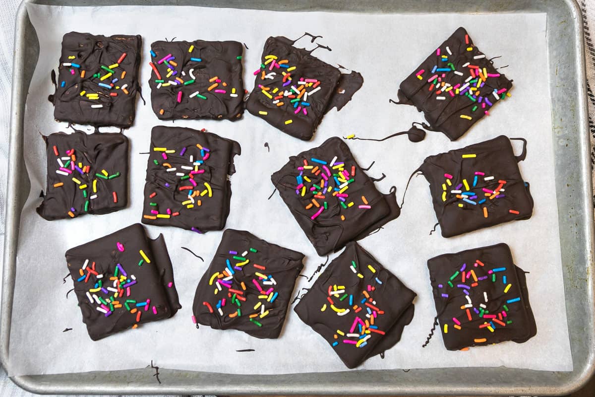 Twelve chocolate covered graham cracker squares on a baking sheet lined with parchment paper.