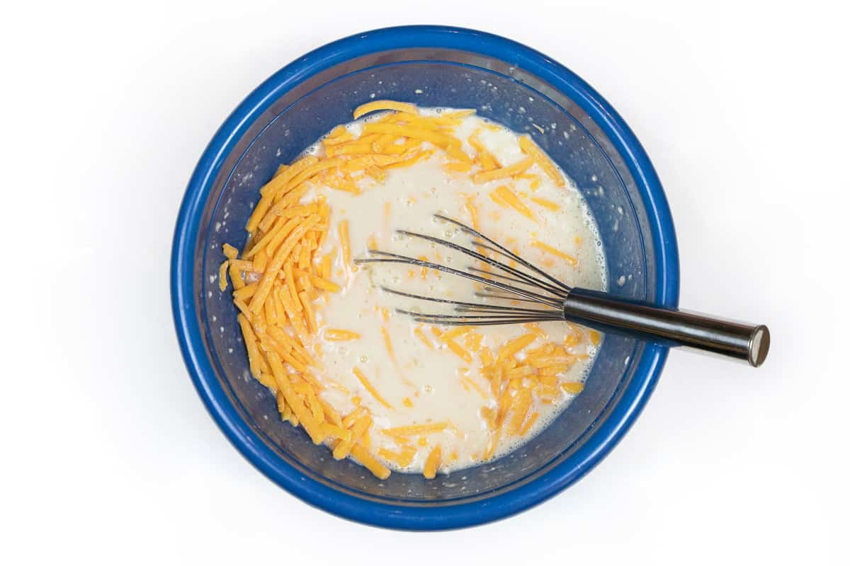 Cheddar cheese is added together with the Bisquick mix, milk, and eggs in the bowl.