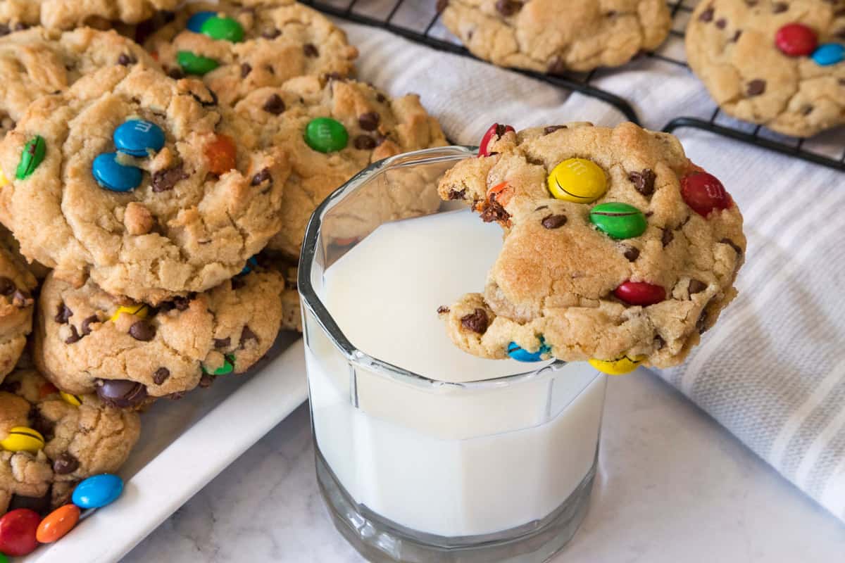 Chocolate chip M&M cookies on a plate with a glass of milk.