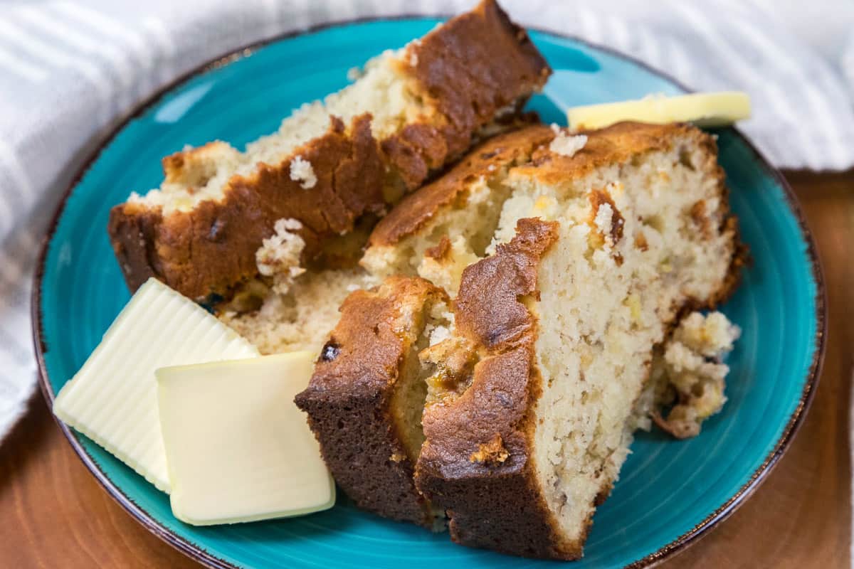 Four slices of banana bread with cream cheese on a plate with butter slices on the side, but without chocolate chips.