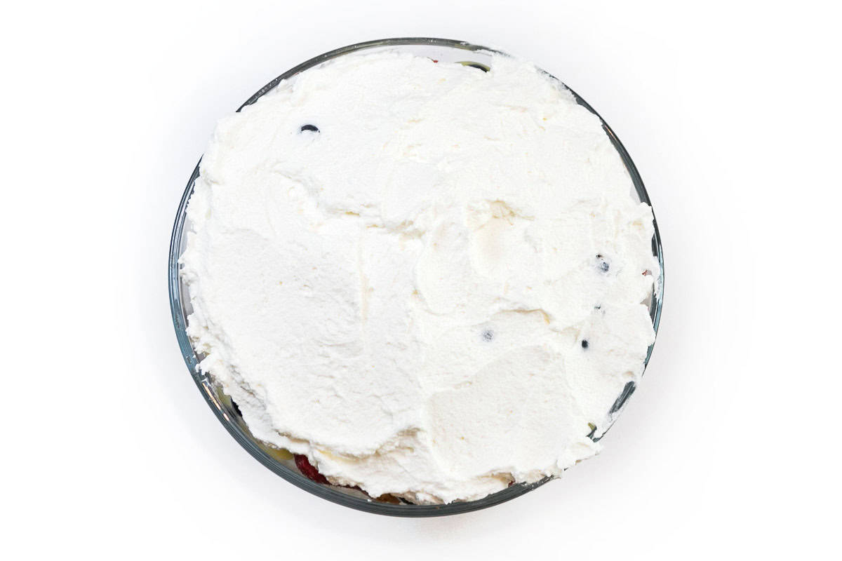 Whipped cream is spread on top of the trifle dessert.