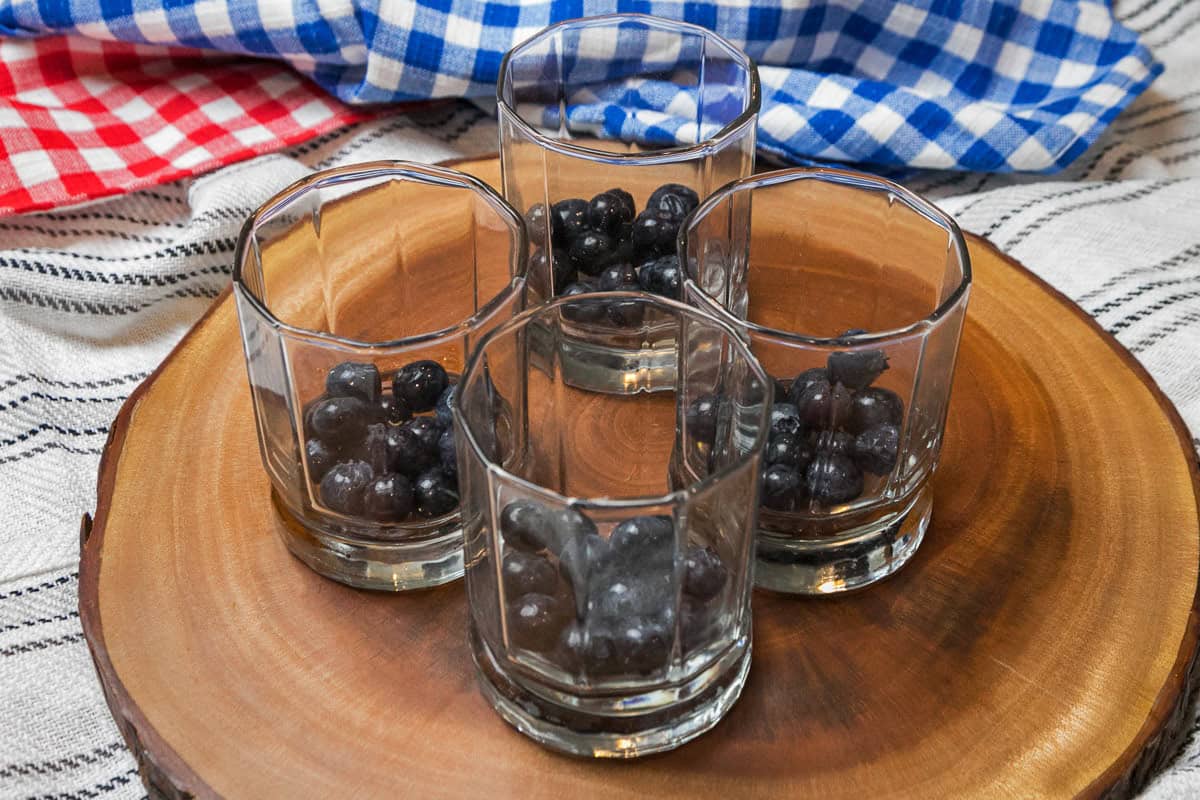 Four glasses with blueberries on the bottom.