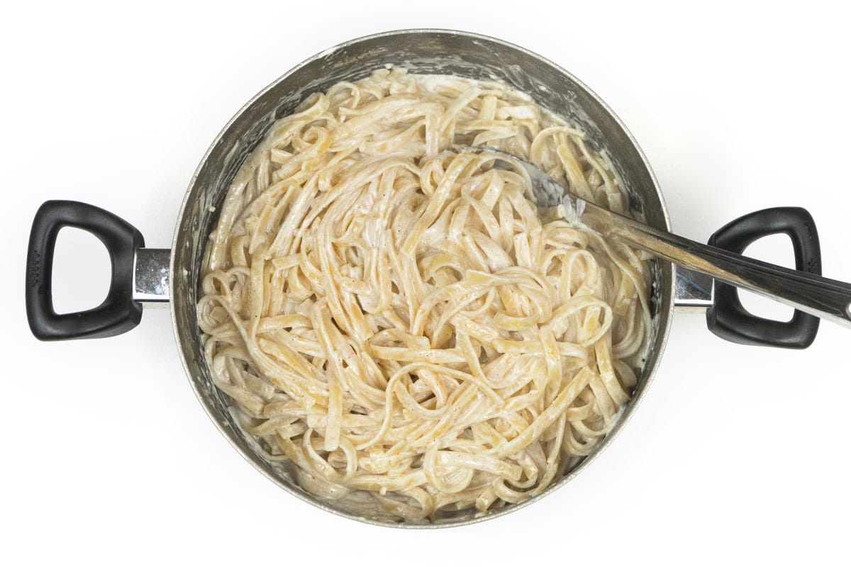 Alfredo sauce and fettuccine noodles in a large pot.