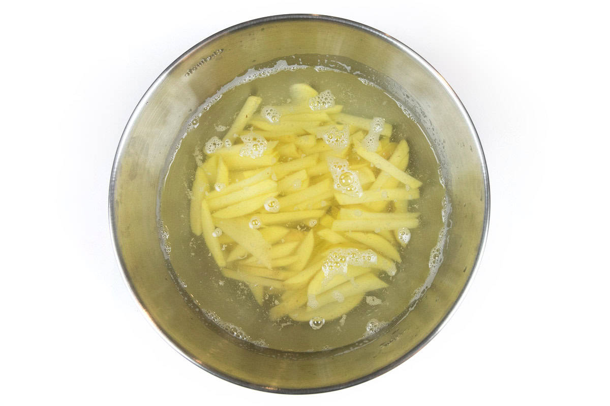 Sliced potatoes in a bowl of cold water.