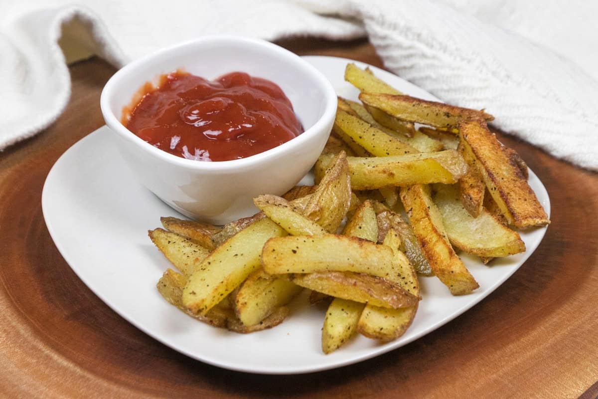 Crispy oven baked French fries on a plate with ketchup.