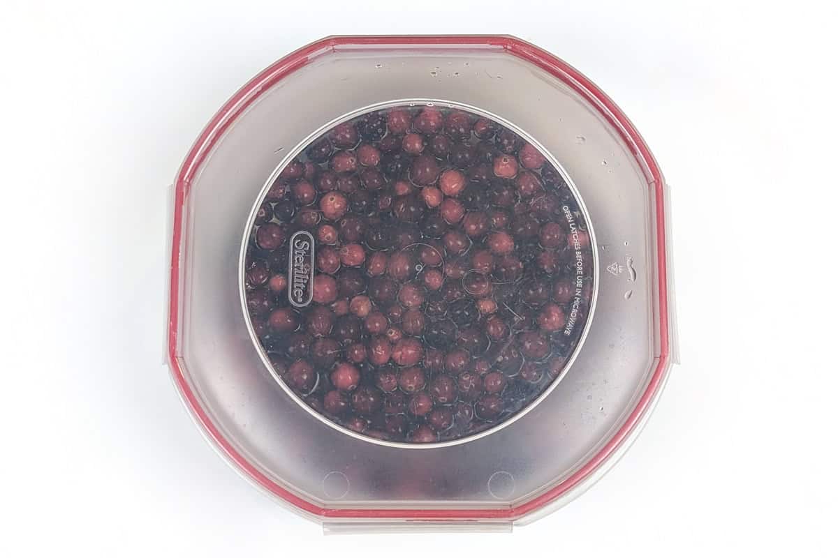 Fresh cranberries, soda pop, and apple cider juice in a bowl with a lid on it.