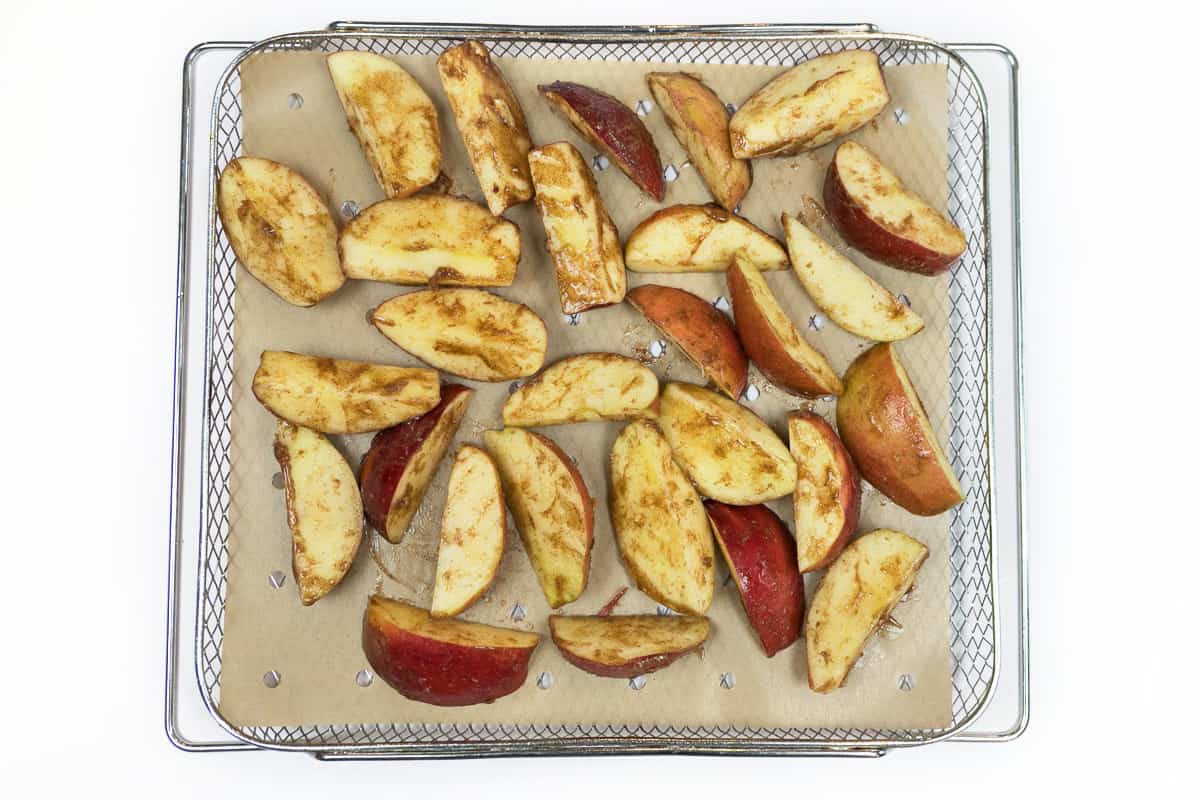 Apple slices on parchment paper in the air fryer basket.