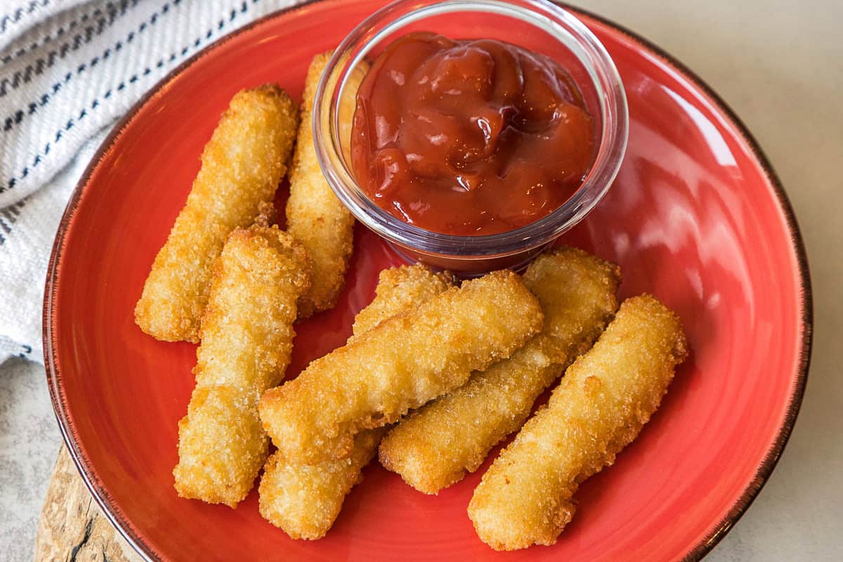 Crispy air fryer fish sticks on a plate with ketchup.