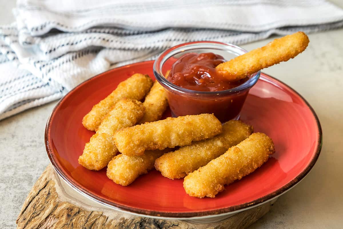 Air fryer fish sticks (frozen) on a plate with dipping ketchup.