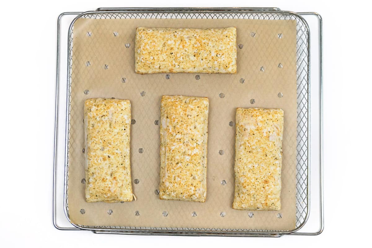Parchment paper with holes in it and frozen hot pockets are placed on the fryer basket in a single layer.