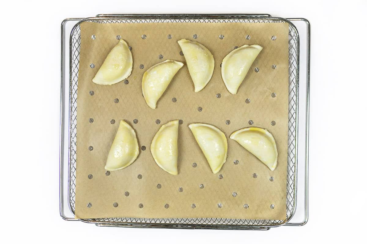 Eight potato and cheese pierogies are placed on the parchment paper.