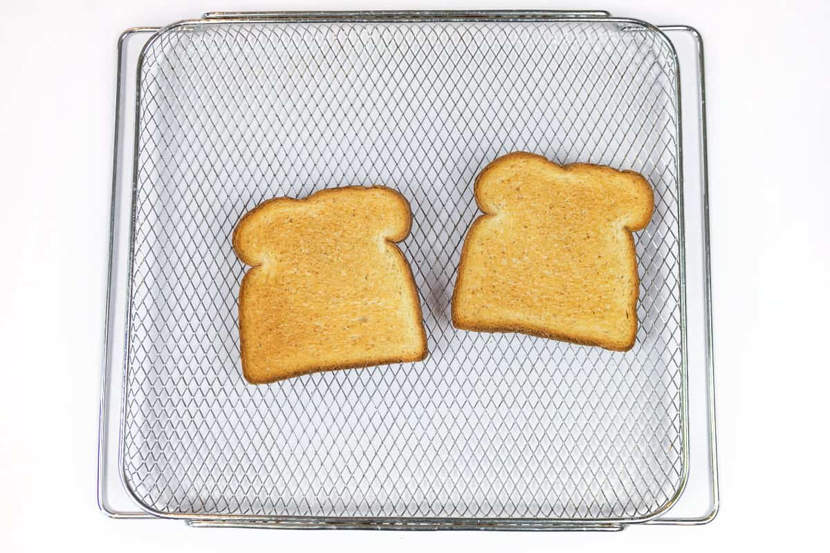 Two slices of bread on the air fryer basket after toasting.