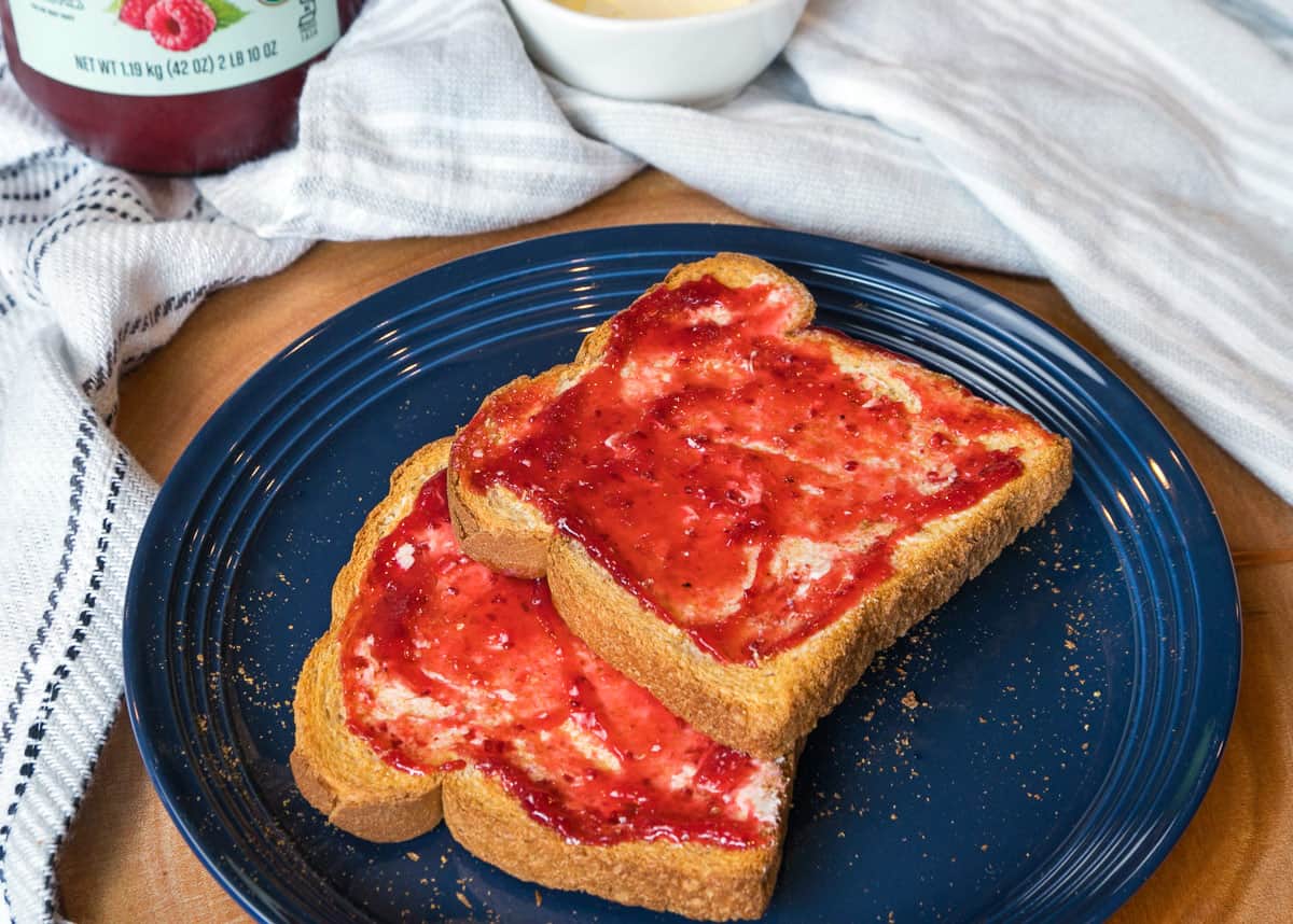 Two slices of air fryer toast with butter and jam on a plate.