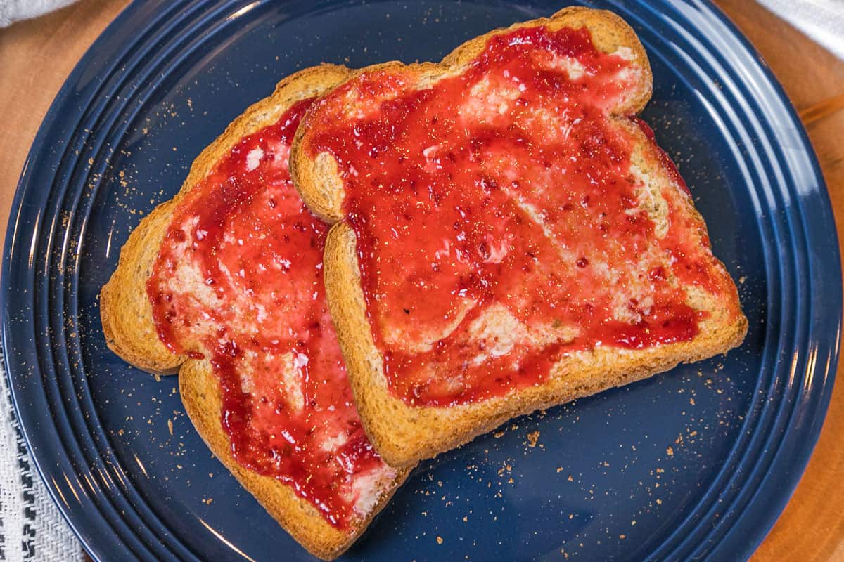 Two slices of air fryer toast with butter and jam on a plate.