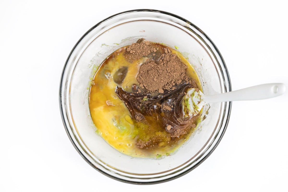 Unsweetened cocoa powder, honey, eggs, vanilla extract, and mashed avocado in a bowl.