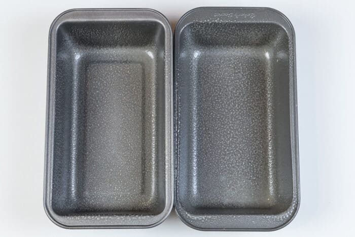 Two loaf pans sprayed with cooking oil.