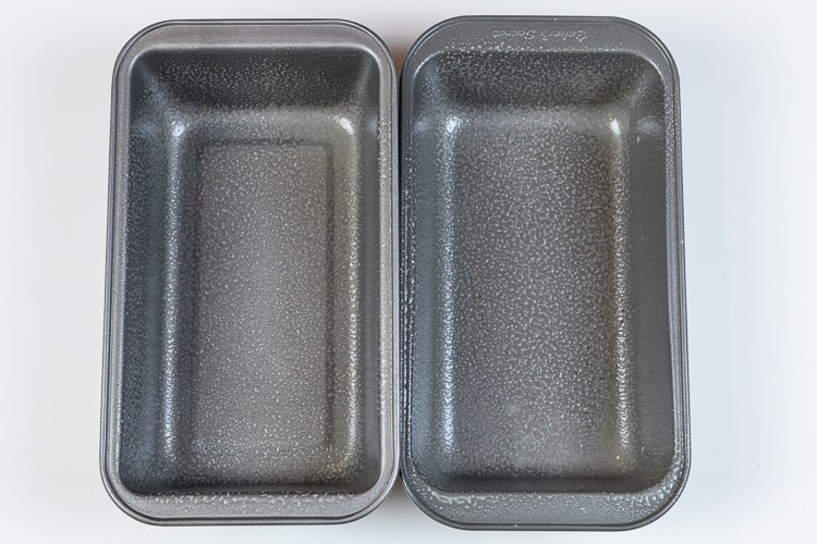 Two loaf pans are sprayed with non-stick cooking spray.