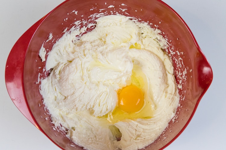 One egg is added to the melted butter, cream cheese, and sugar mixture in the bowl.