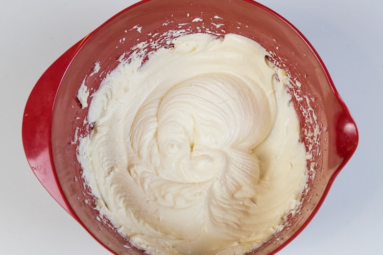 One egg is mixed together with the melted butter, cream cheese, and sugar mixture in the bowl.