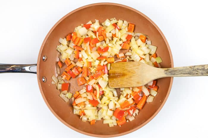 The garlic and sugar are added to the onions and red bell peppers in the frying pan.