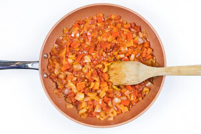 The tomatoes, salt, and pepper are added to the onions and red bell peppers in the frying pan.