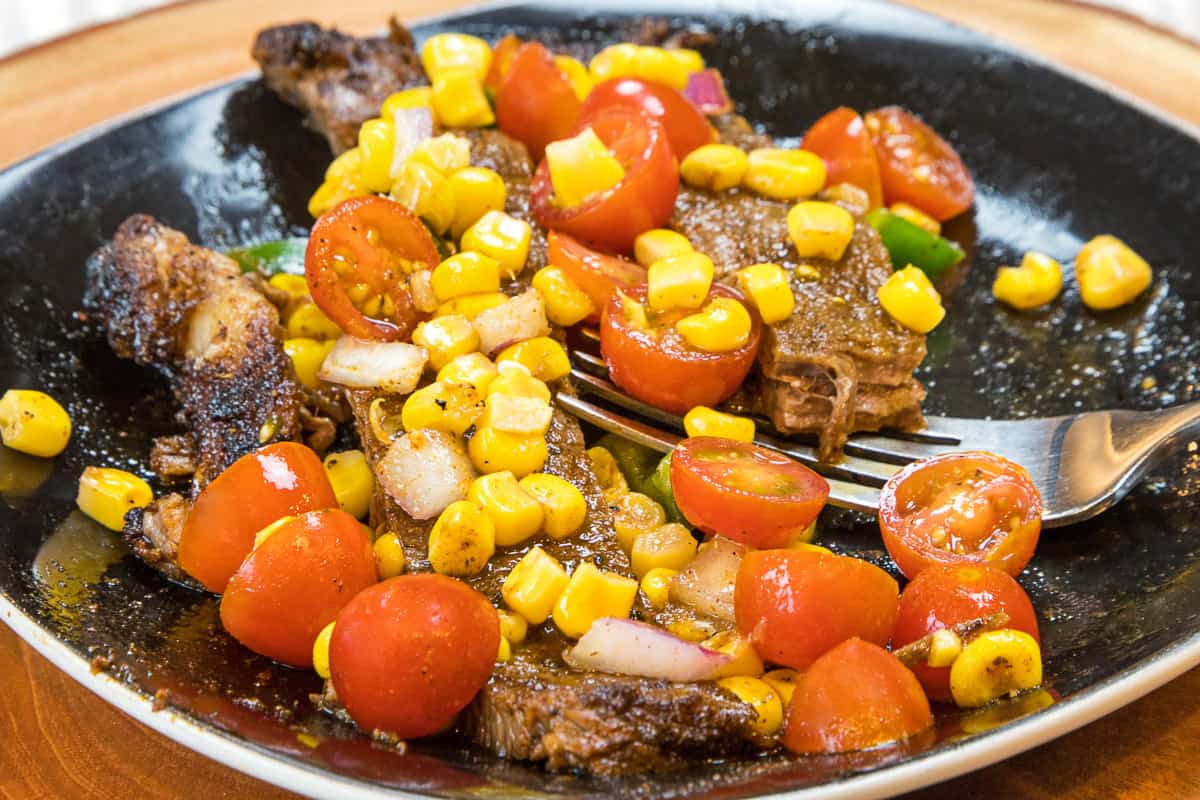 Flank steak on a plate topped with roasted corn salsa.