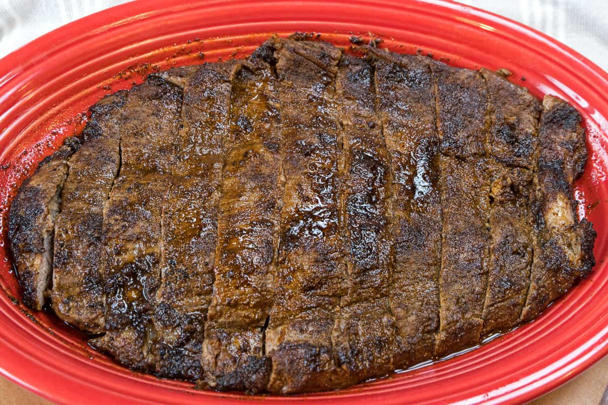 Broiled flank steak cut against the grain in strips on a plate.