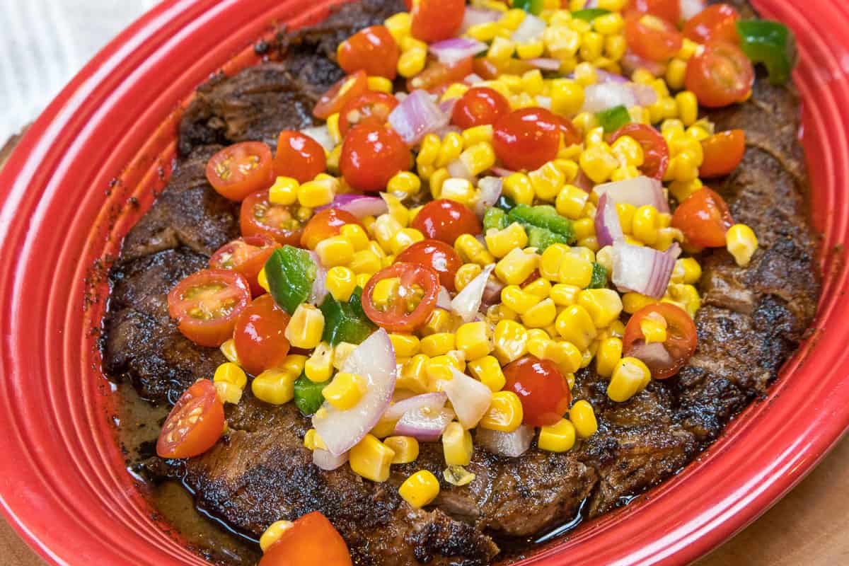 Broiled flank steak on a plate with roasted corn salsa on the top.