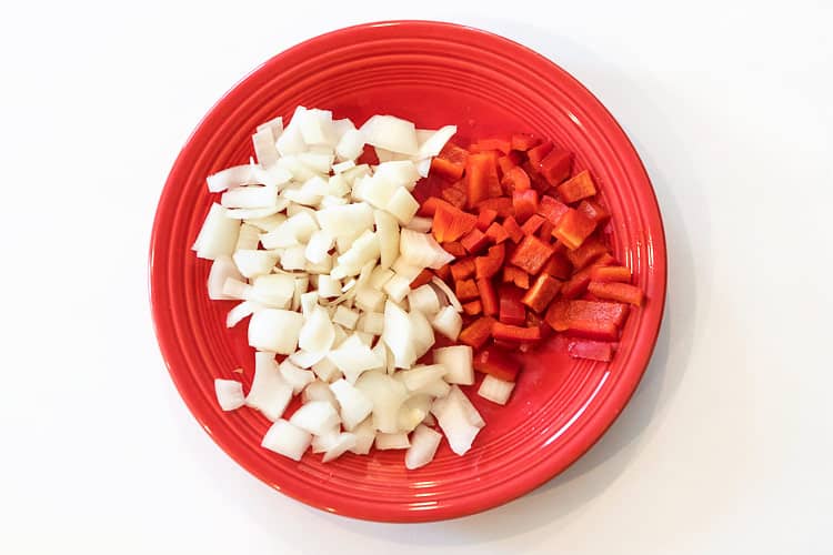 One diced red pepper and one diced onion on a plate for chicken & noodle casserole.