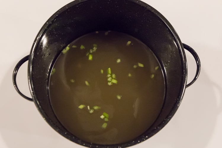 Pot of chicken broth with water and celery.