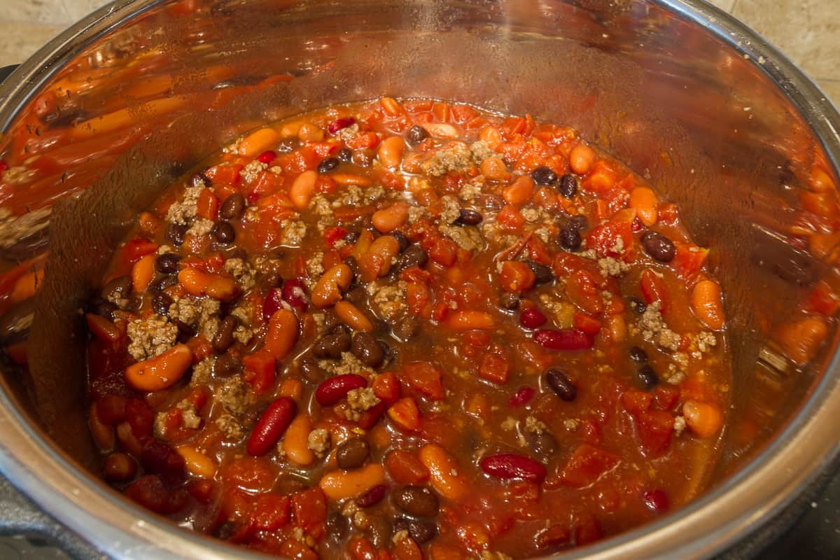 The kidney beans, chili beans, black beans, and diced tomatoes are added to the ground beef.
