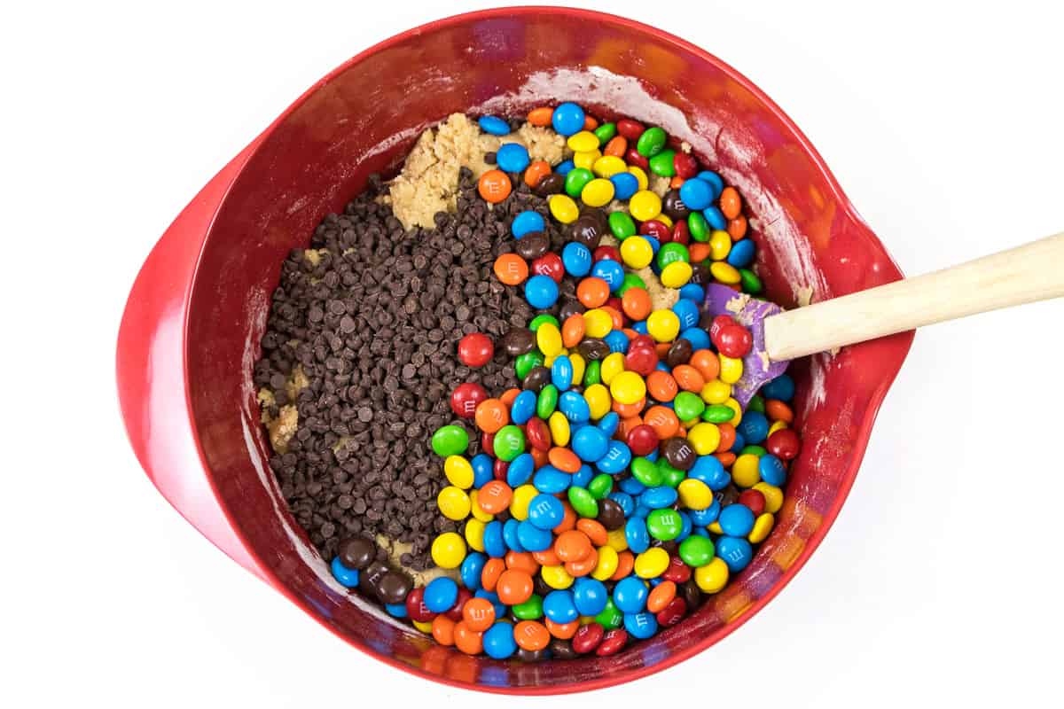 M&M's and chocolate chips are added to the flour mixture, eggs, vanilla extract, softened butter, sugar, and light brown sugar.