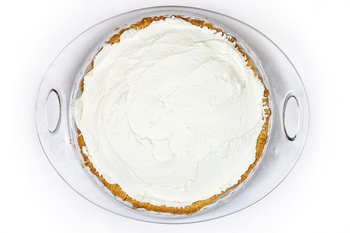 Whipped cream is spread on top of the chocolate pie.