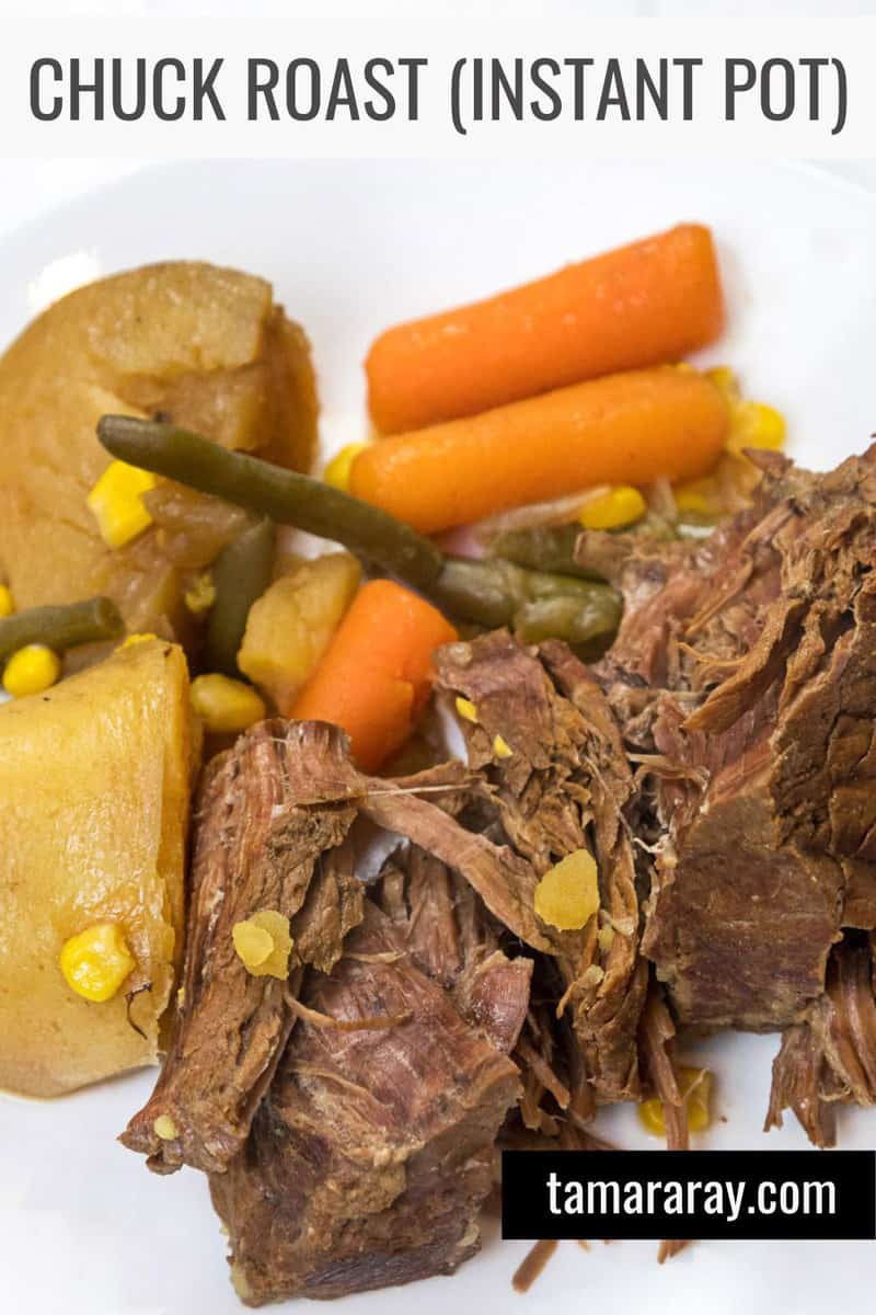 Chuck roast on a plate with potatoes, onions, carrots, corn, and green beans.