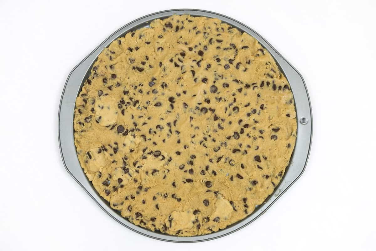 Chocolate chip cookie dough on a pizza pan.