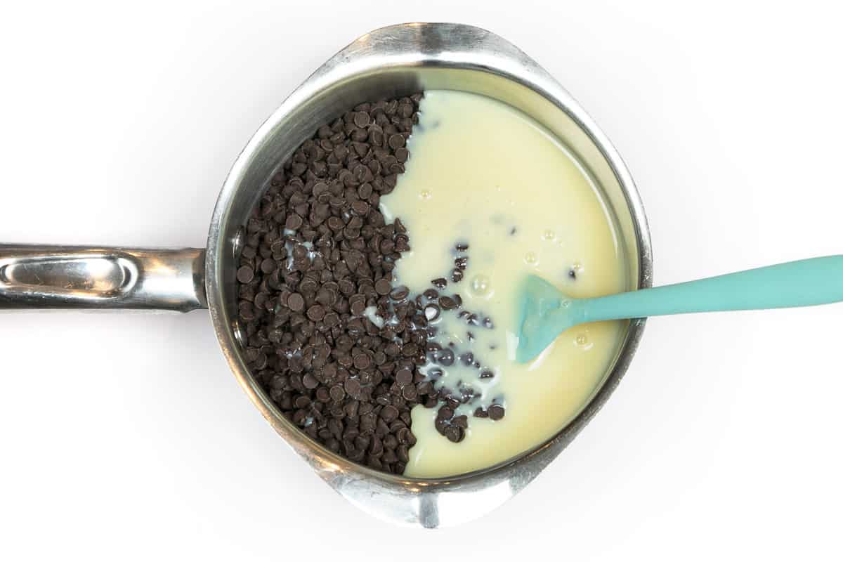 Mini semi-sweet chocolate chips and sweetened condensed milk in a saucepan.