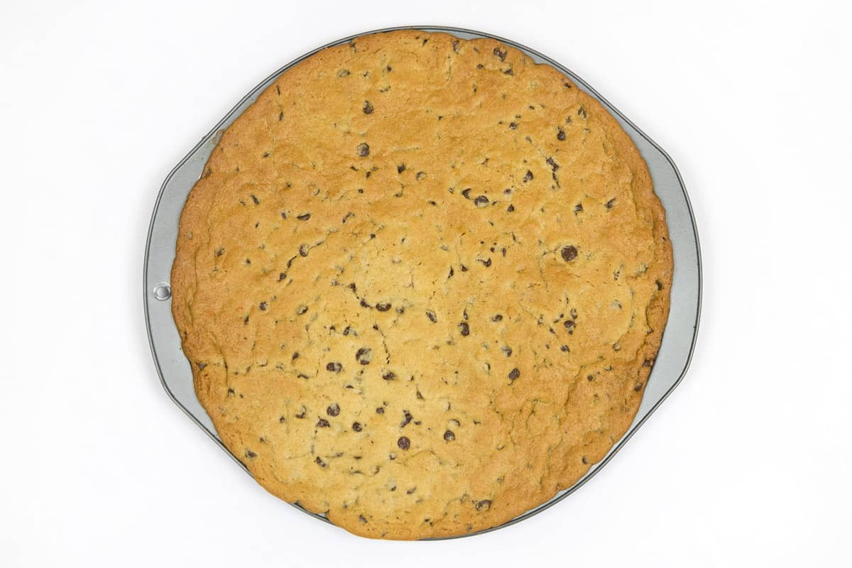 A baked chocolate chip cookie on a pizza pan.