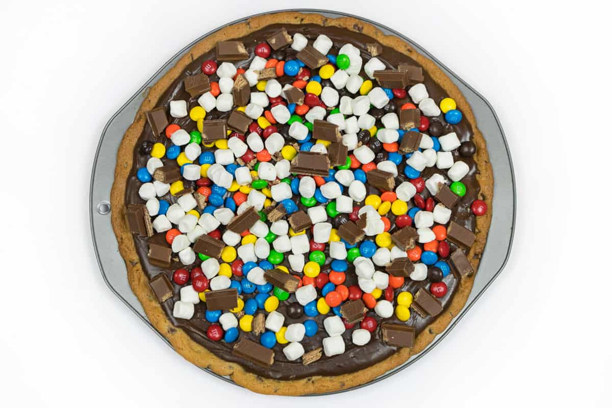 A layer of M&M's milk chocolate candy, Kit Kat pieces, and mini marshmallows on the cookie pizza.