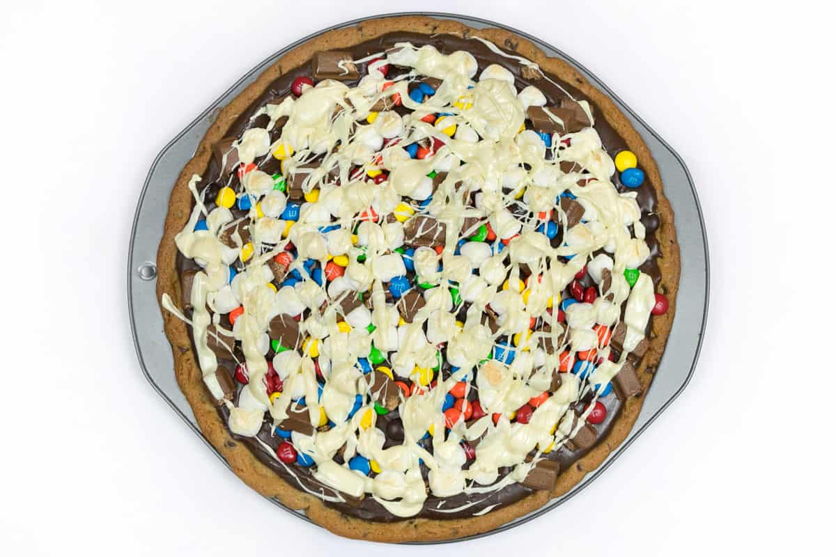 The melted white chocolate is drizzled on top of the cookie pizza.