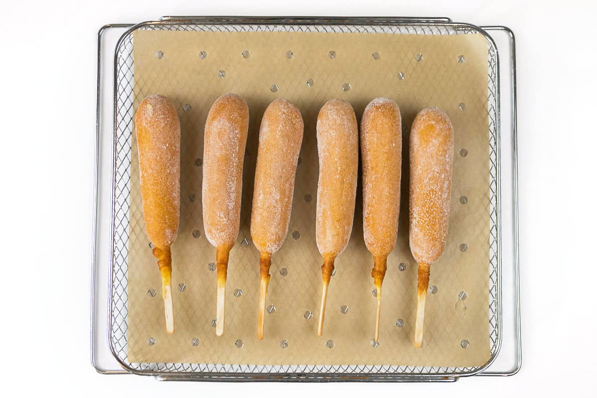 6 corn dogs on the air fryer basket in a single layer over parchment paper with holes in it.