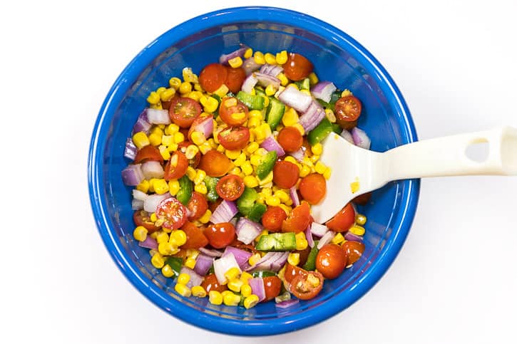 Corn, tomatoes, jalapeño peppers, and red onions in a bowl seasoned with salt, pepper, and lemon juice.