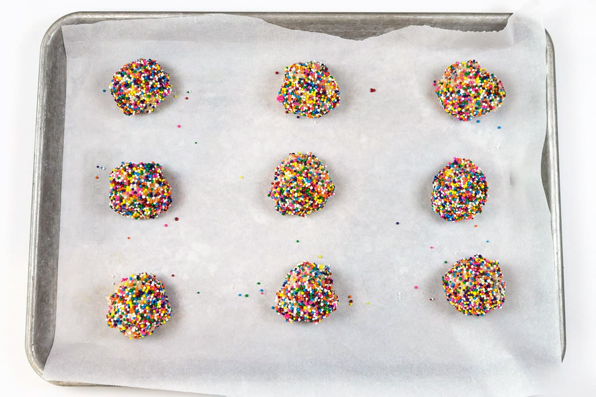 Nine balls of cookie dough with sprinkles are put on the cookie sheet lined with parchment paper. Place the balls of cookie dough two inches apart on the cookie sheet.