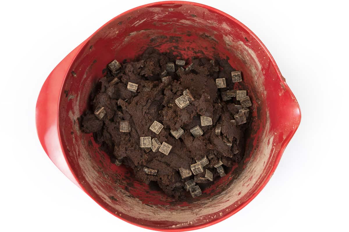 Dark chocolate chip chunks are added to the cookie dough in the bowl.