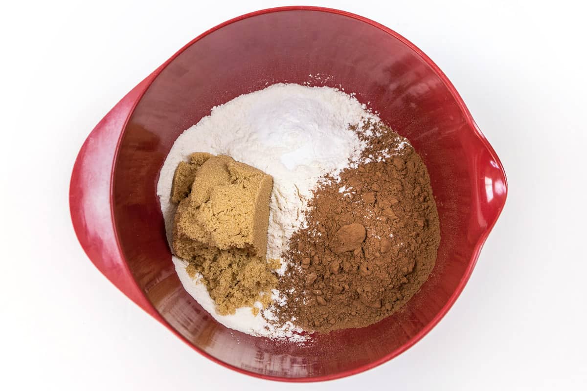 Flour, brown sugar, cocoa powder, baking soda, baking powder, and salt are added to a bowl.