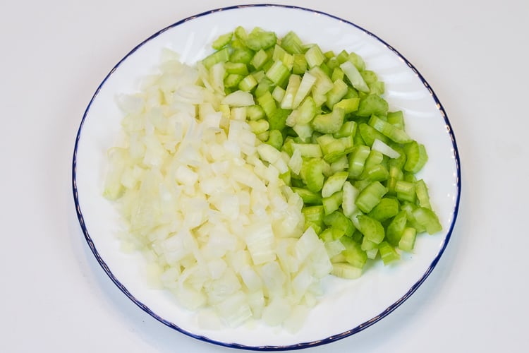 Diced onion and celery sticks on a plate for the Thanksgiving dressing.