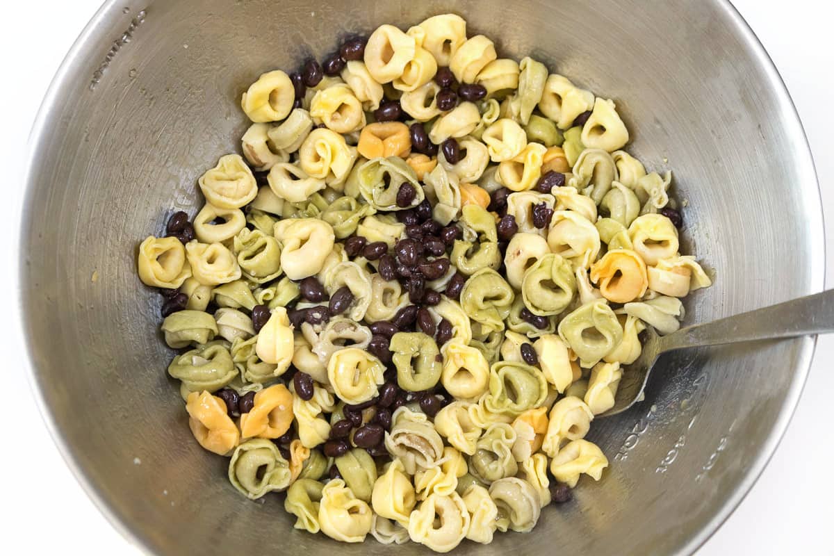 The tortellini is added to the black beans and olive oil.