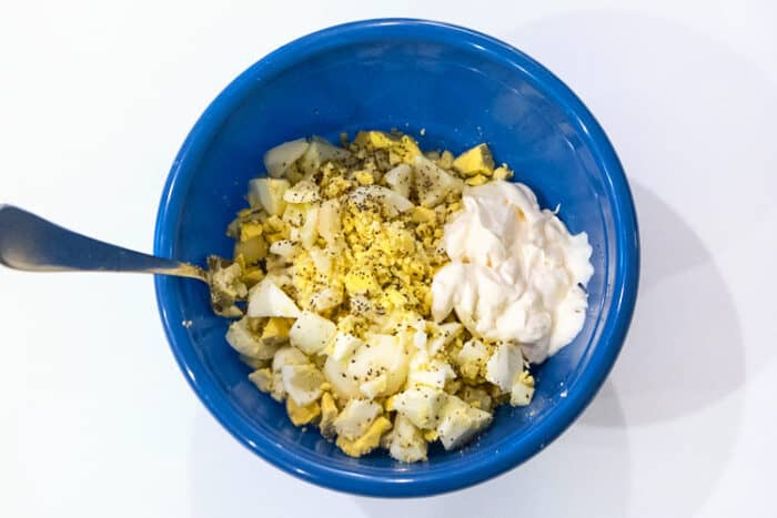 Mayonnaise, salt, pepper, lemon juice, and hard-boiled eggs in a bowl.