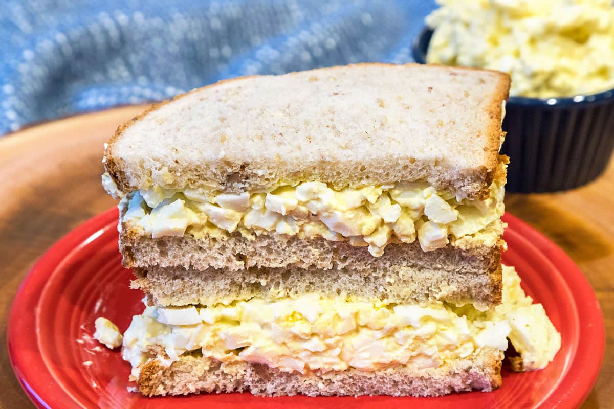 Egg salad between two pieces of wheat bread on a plate.